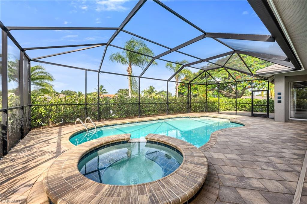 Screened outdoor living area featuring a freeform swimming pool, integrated spa, and paver decking