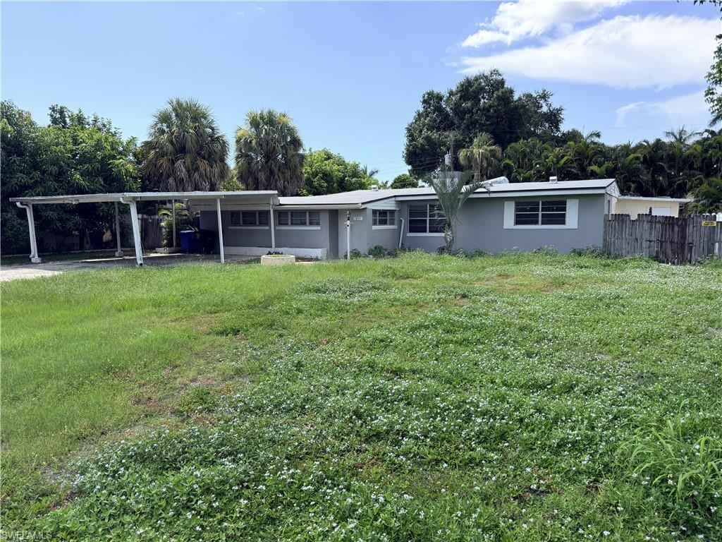 Single-story residence featuring a carport, multiple windows, and a partially fenced yard