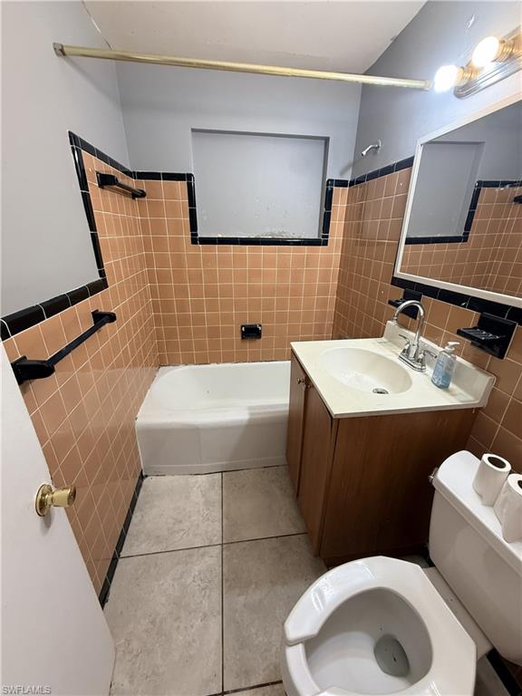 Bathroom featuring a built-in tub, a vanity with a white countertop and base cabinet, and tiled walls with black trim