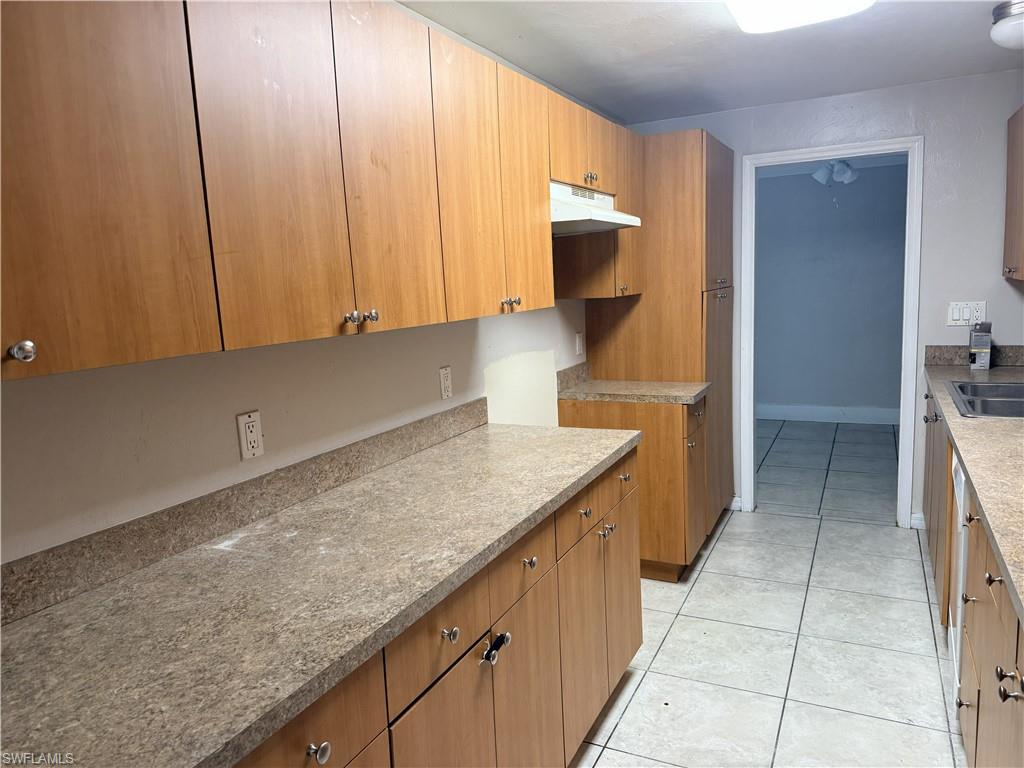 Kitchen featuring light wood-finish cabinetry, speckled countertops, tile flooring, and a stainless steel sink