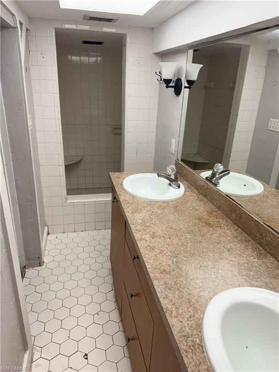 Bathroom featuring a dual-sink vanity with wood-finish cabinetry, a large vanity mirror, hex-tile flooring, and a tiled shower with a built-in bench