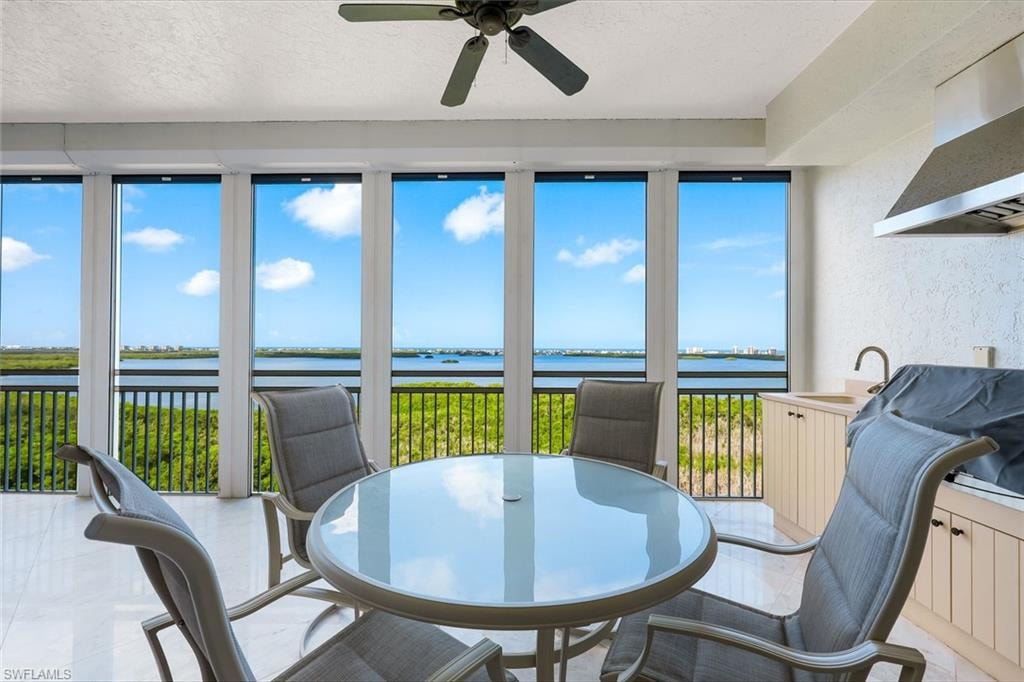 Expansive balcony featuring floor-to-ceiling windows, a ceiling fan, a built-in outdoor kitchen with sink, and a water backdrop