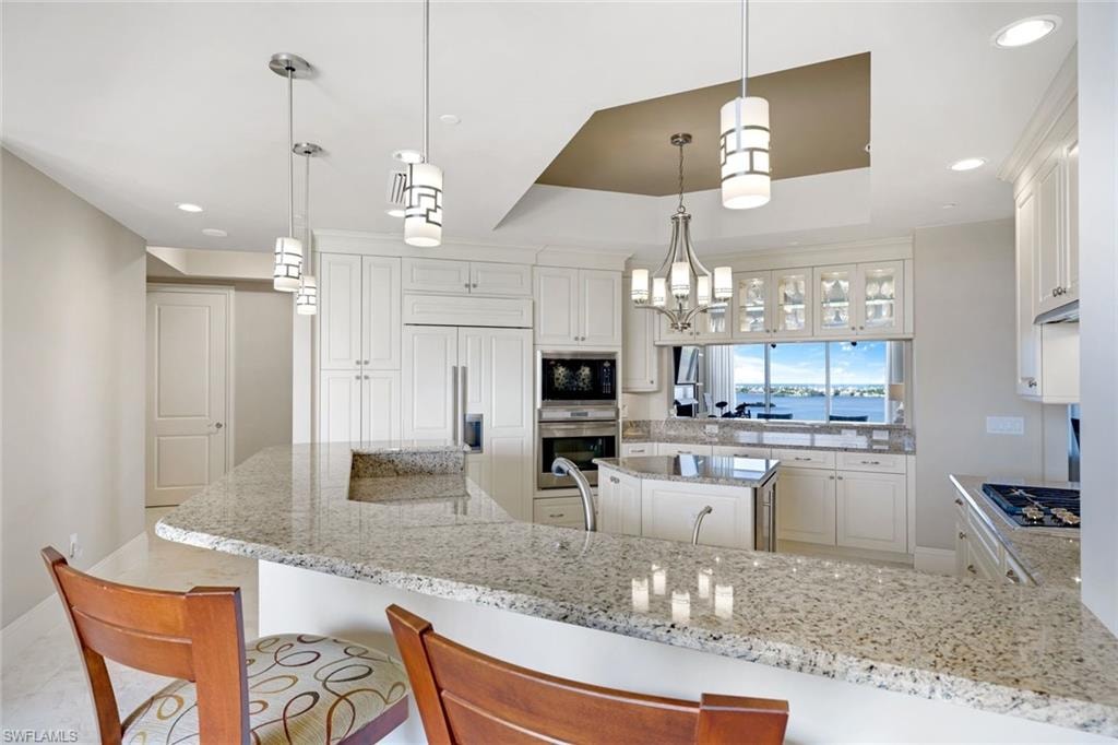 Gourmet kitchen featuring white cabinetry with glass-front uppers, quartz countertops, stainless steel appliances including dual ovens and gas cooktop, pendant lighting, and an oversized island with seating