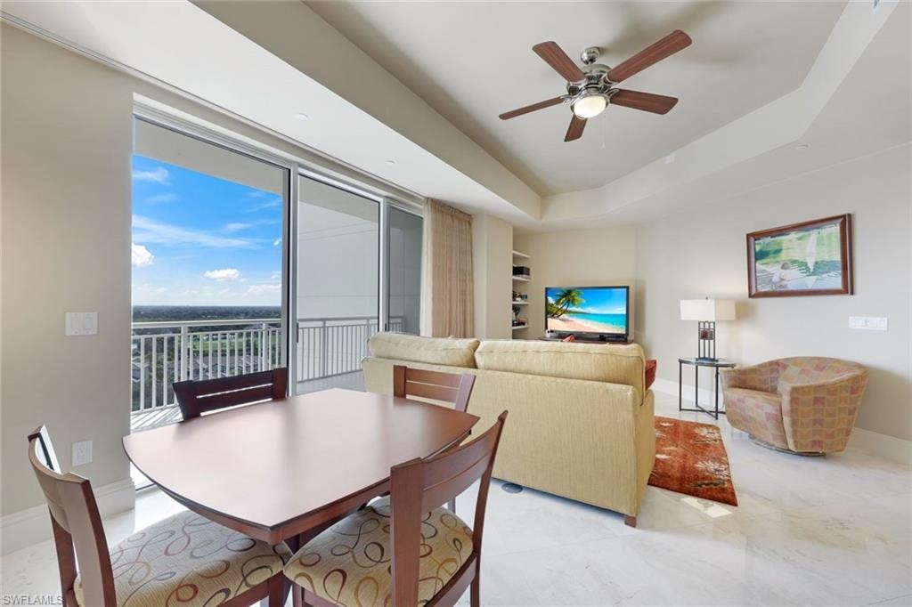 Expansive sliding glass doors leading to a balcony with metal railings, tray ceiling, recessed lighting, and a ceiling fan with light fixture