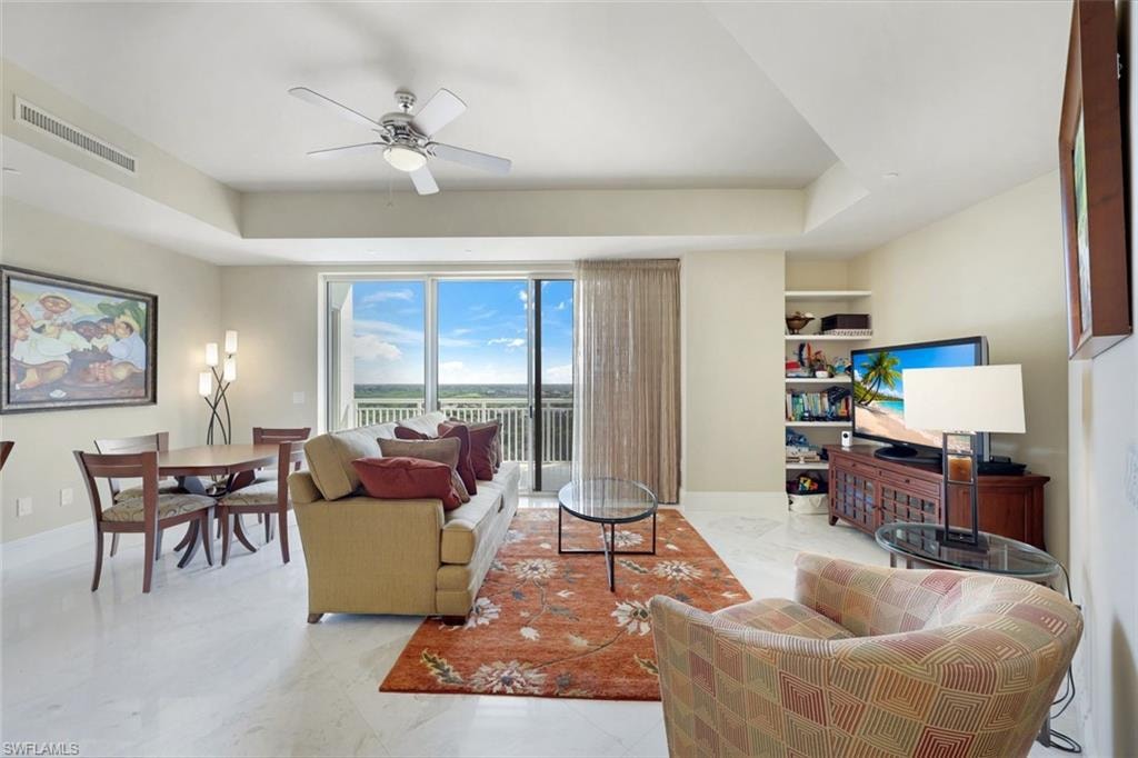 Spacious open-concept living area featuring floor-to-ceiling sliding glass doors with panoramic outlooks, ceiling fan, built-in shelving and cabinetry, neutral wall-to-wall flooring, and abundant natural light throughout