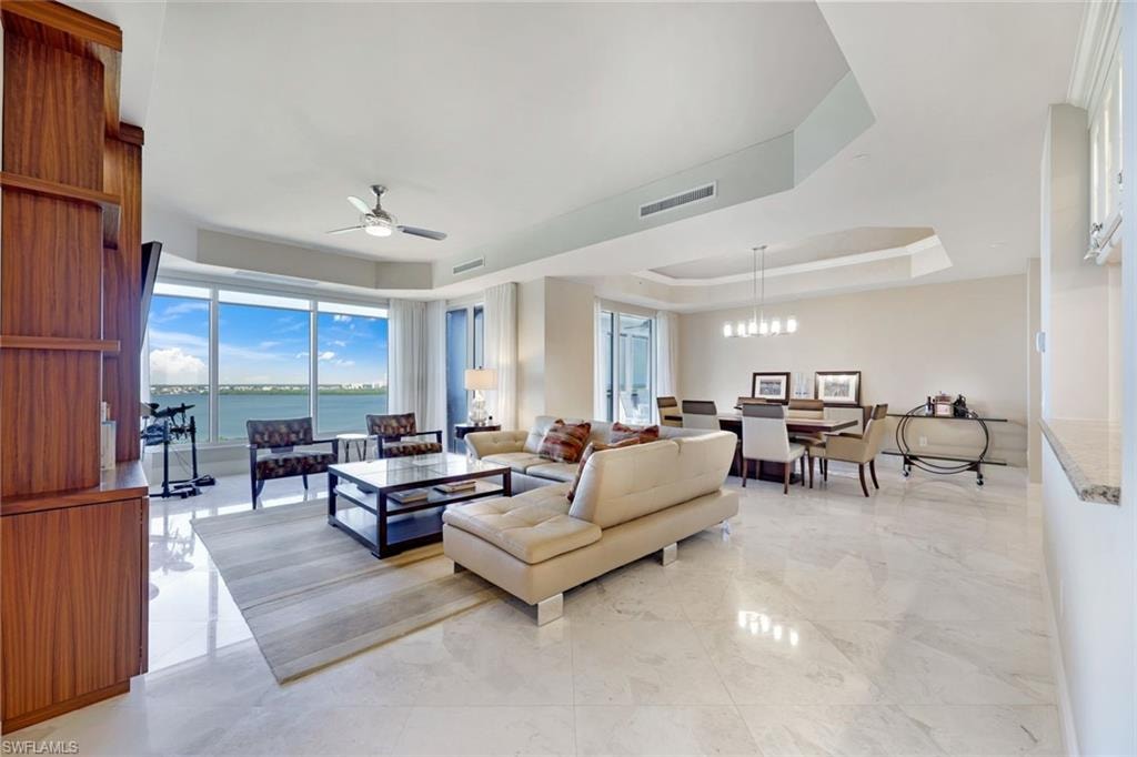 Expansive open-concept living area featuring polished stone flooring, floor-to-ceiling windows with panoramic vistas, coffered ceiling with recessed lighting, and a ceiling fan