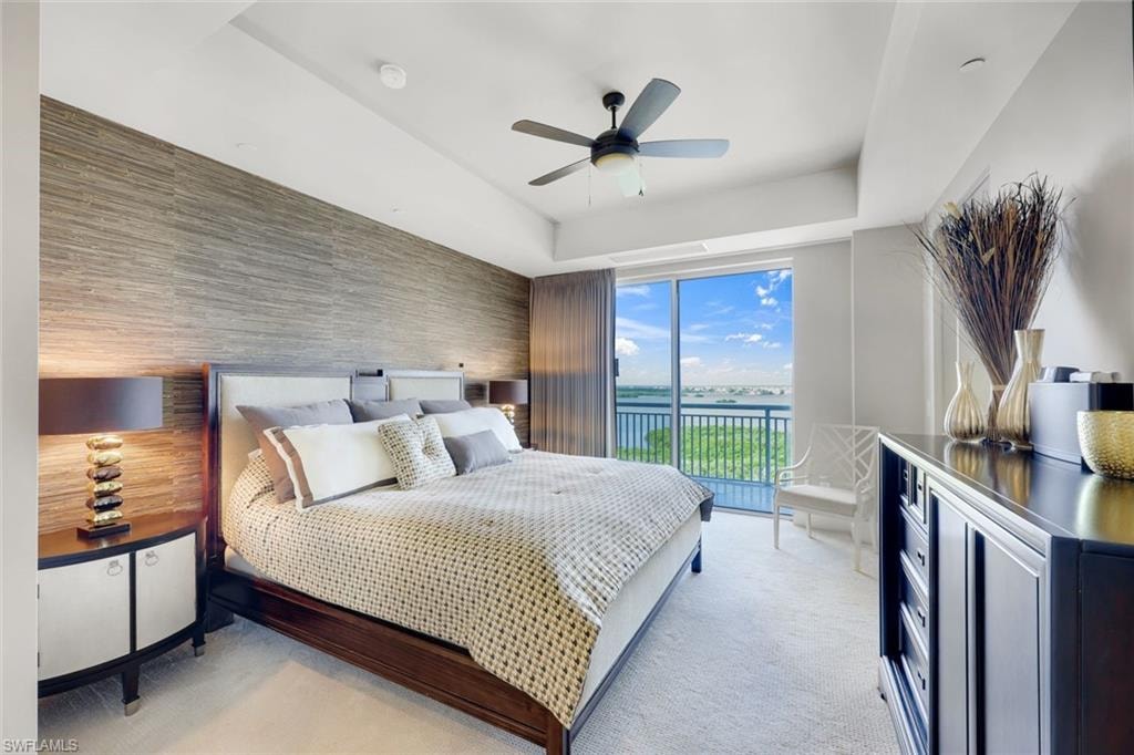 Master bedroom with floor-to-ceiling glass doors opening to a private balcony with scenic vistas, ceiling fan, wood-finish nightstands with integrated lighting, neutral carpet flooring, white ceiling with recessed lighting, and a black dresser with polished metal hardware