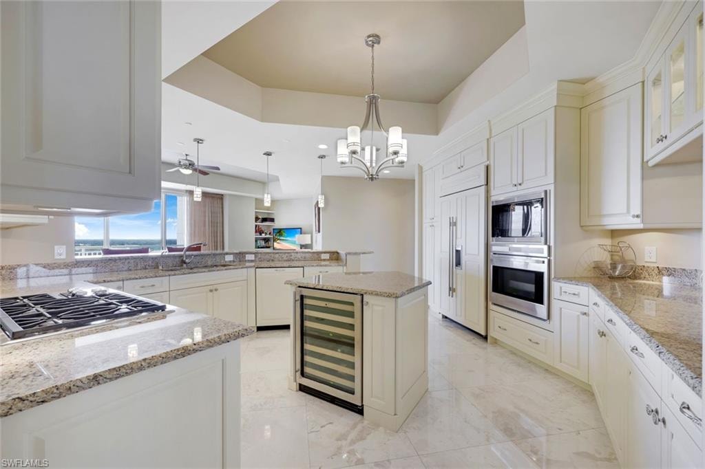 Gourmet kitchen featuring white cabinetry, granite countertops, professional-grade gas cooktop, stainless steel appliances, a central island with wine refrigerator, recessed and pendant lighting, and polished stone flooring throughout