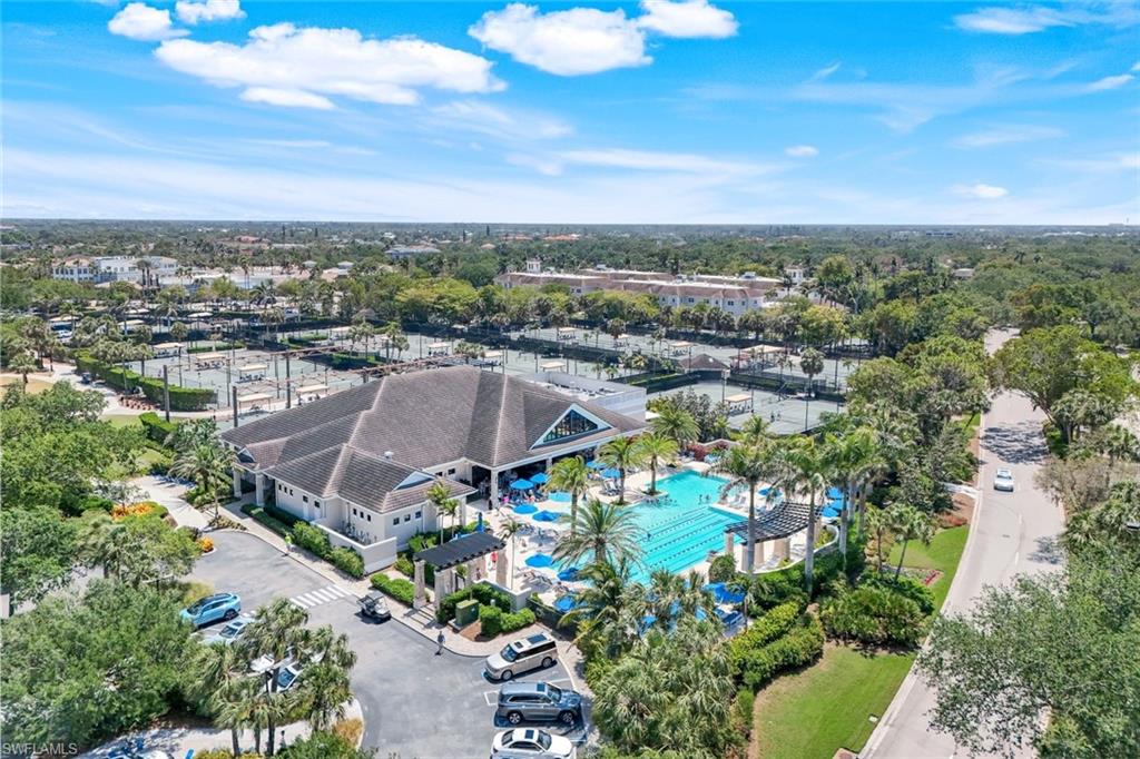 Resort-style aquatic center featuring multiple swimming pools with vibrant blue water, surrounding sun deck with mature landscaping, and a modern clubhouse structure