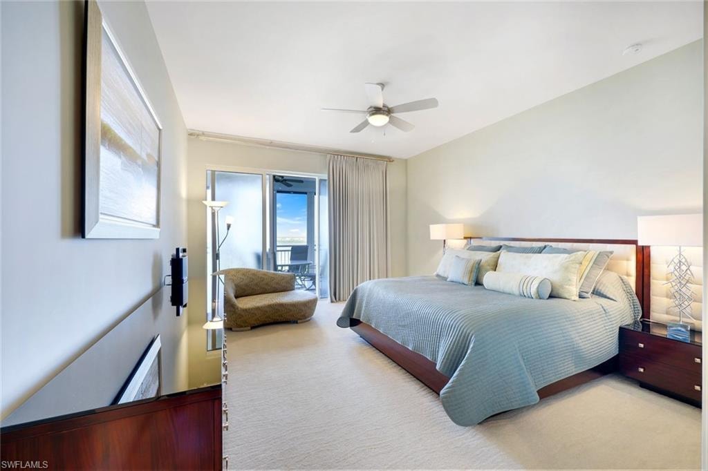 Spacious master bedroom suite featuring a wood-finish bed frame, layered bedding in soft blue tones, dual nightstands with task lighting, ceiling fan with integrated light fixture, and direct access to a private balcony