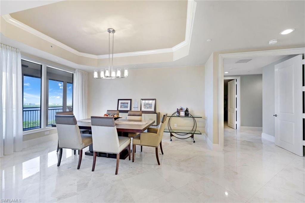 Elegant open-concept dining and living area featuring polished light-stone flooring, a tray ceiling with recessed lighting, and floor-to-ceiling windows with water views