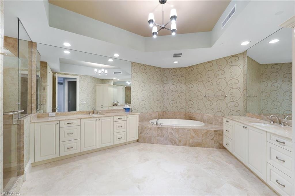 Dual vanities with integrated sinks, recessed lighting, a built-in soaking tub, a glass-enclosed shower, and tile flooring