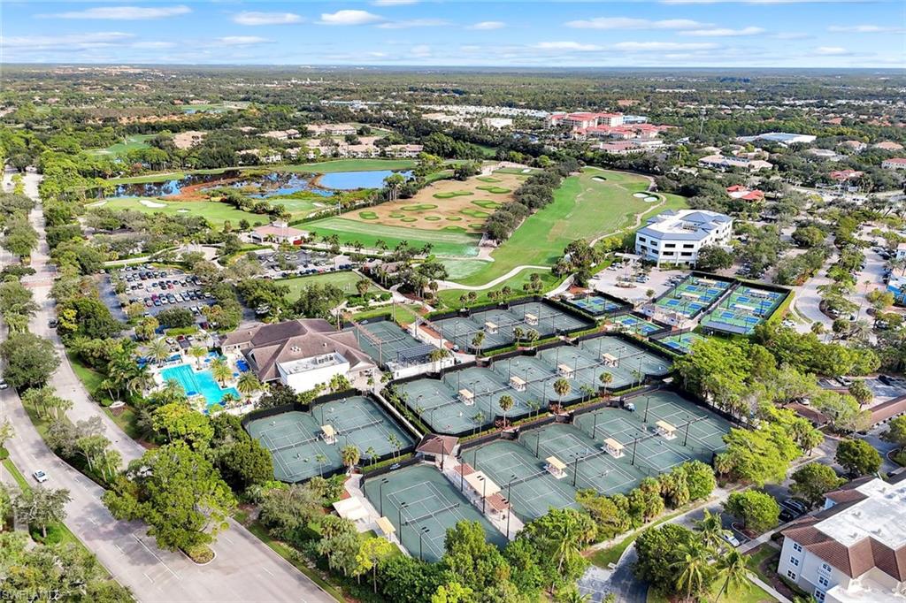 Aerial view showcasing an expansive recreational complex featuring multiple hard courts, resort-style pool with lounging areas, manicured grounds with mature landscaping, and additional sports facilities