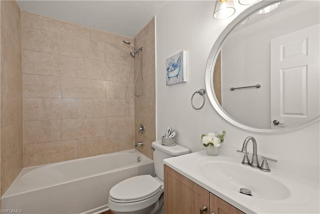 Bathroom featuring a tiled shower surround, white bathtub, vanity with an integrated sink, brushed nickel faucet, and an oval mirror