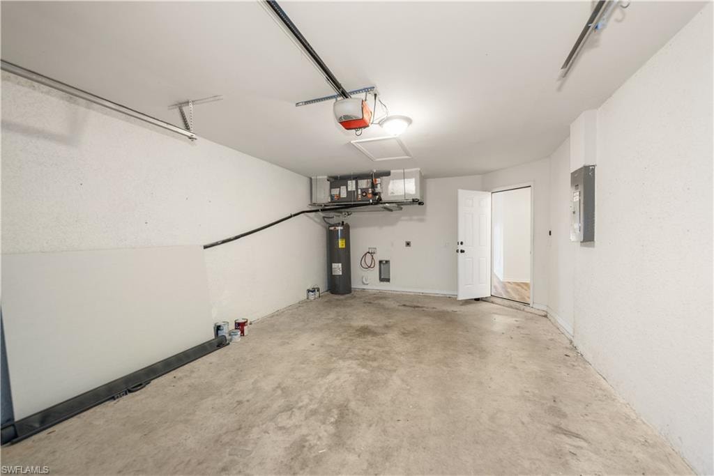 Concrete flooring, white walls, overhead lighting, water heater, and electrical panel