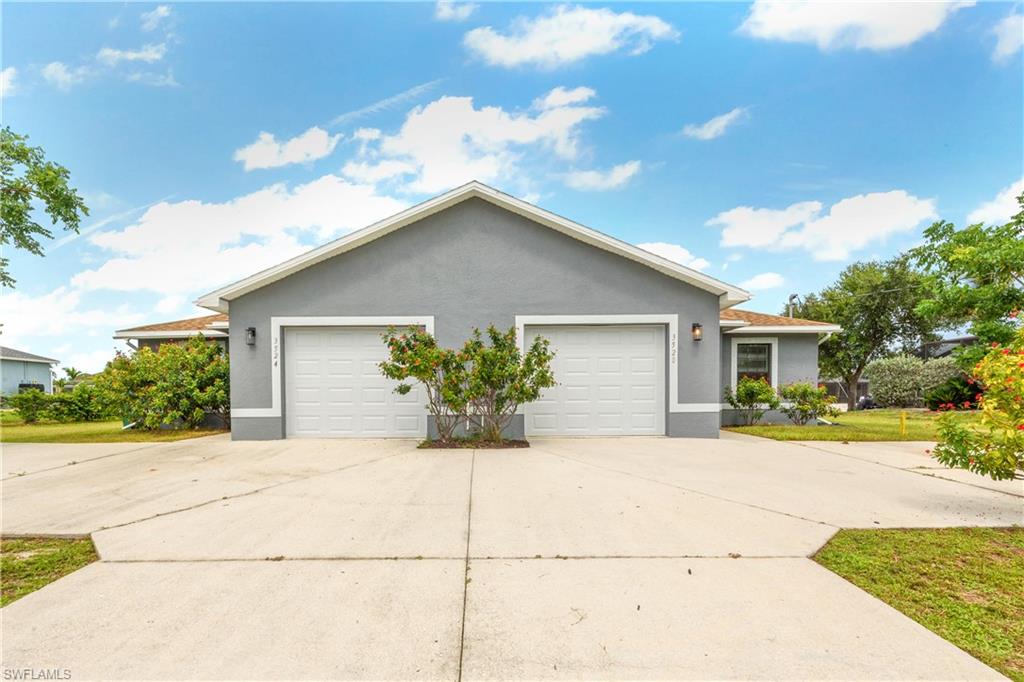 Gray exterior with white trim, two white garage doors, exterior lighting fixtures, and a concrete driveway