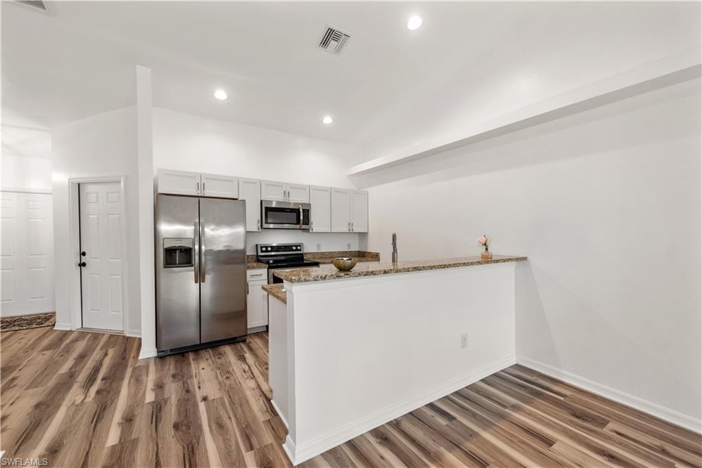 Kitchen featuring wood-finish flooring, white cabinetry, stainless steel appliances, and granite countertops