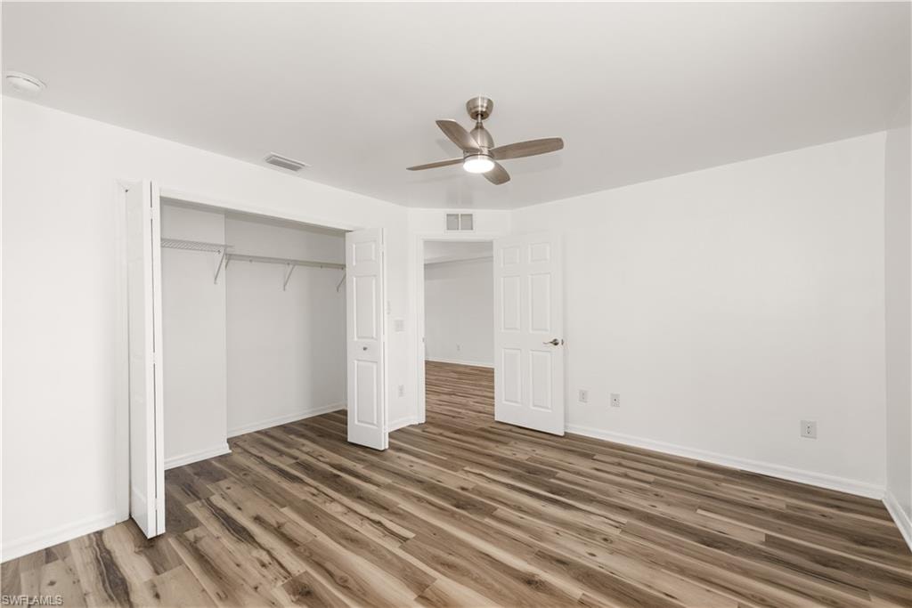 Spacious room featuring wood-finish flooring, white walls, and a ceiling fan