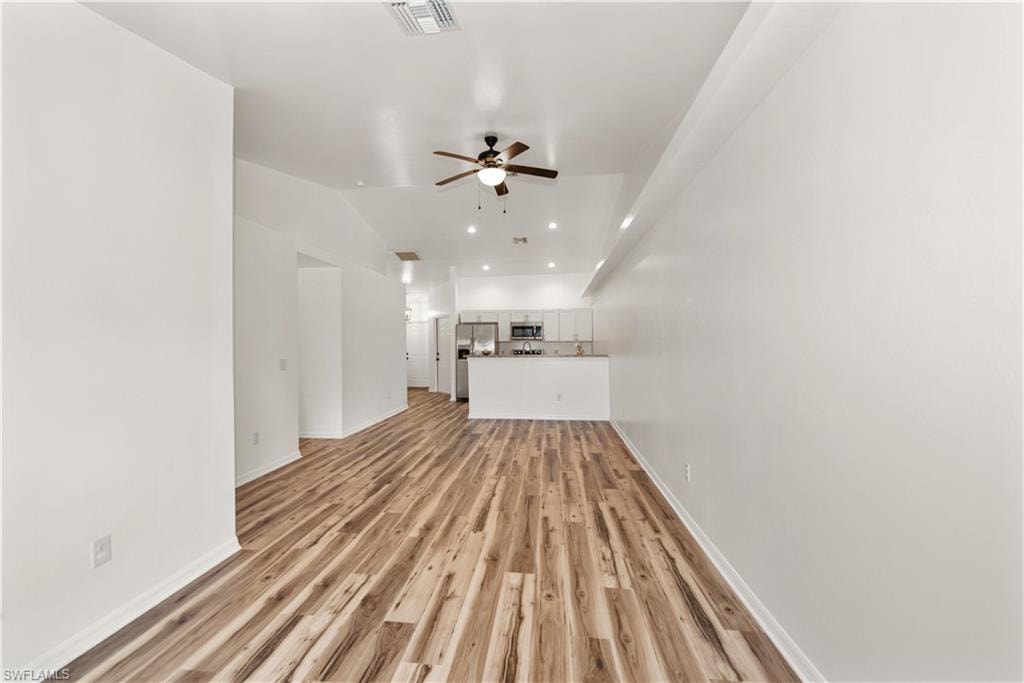 Vaulted ceiling, wood-finish flooring, recessed lighting, ceiling fan, and white cabinetry