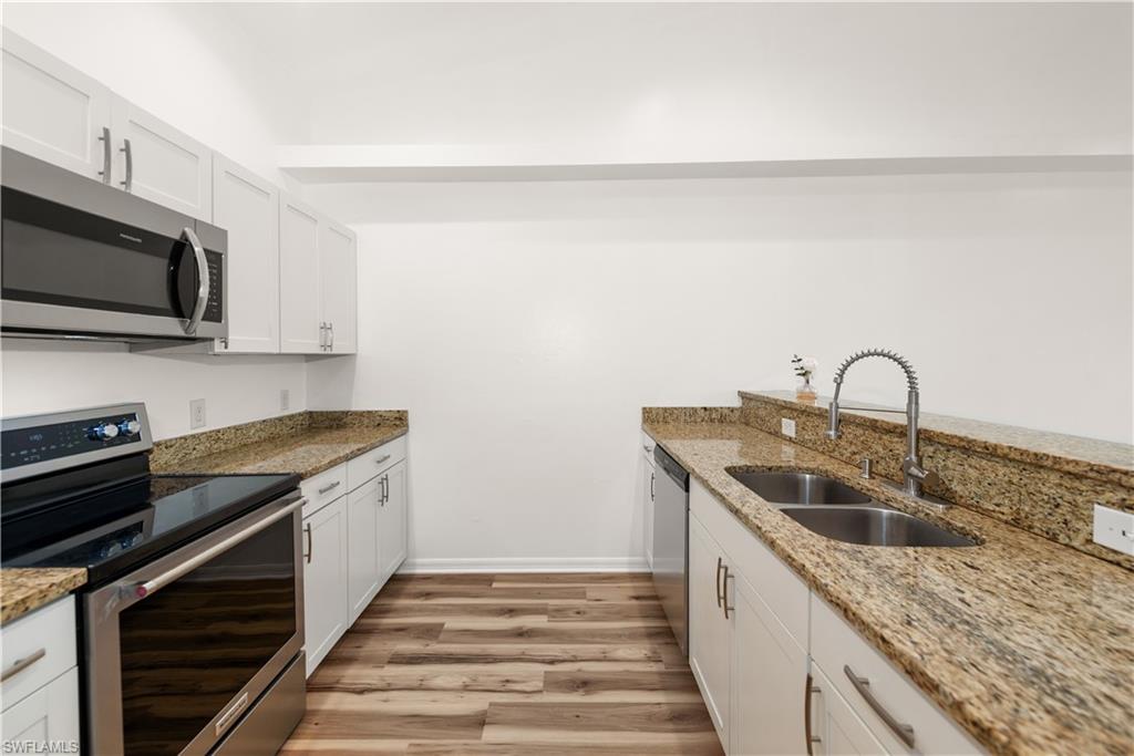 Kitchen featuring white cabinetry, stainless steel appliances, dual basin sink, wood-finish flooring, and light-toned countertops