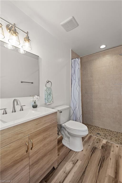 Wood-finish flooring, single vanity with a white countertop, recessed lighting, tile shower surround, and a mosaic tile shower floor