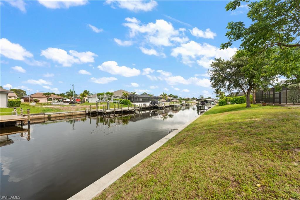 Canal-front property featuring a concrete retaining wall, a private dock structure, and mature trees on a grassy bank