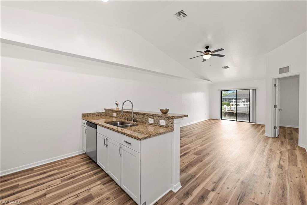 Open-concept living area featuring wood-finish flooring, vaulted ceilings, and a kitchen island with granite countertops and white cabinetry