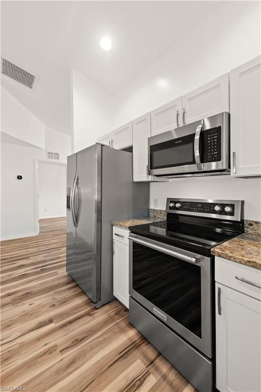Kitchen featuring stainless steel appliances, white cabinetry, wood-finish flooring, and stone countertops
