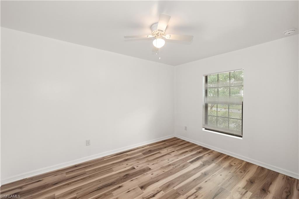 Wood-finish flooring with white baseboards, single window with blinds, and a ceiling fan with integrated lighting