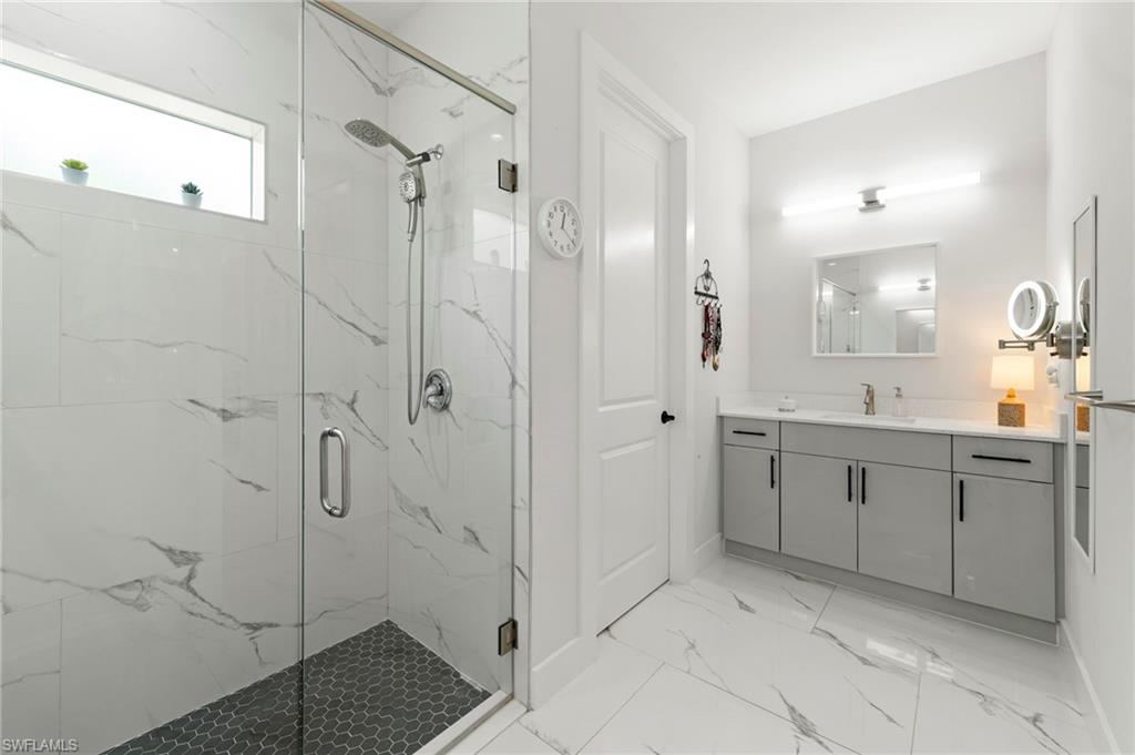 Glass-enclosed shower with a gray hexagonal tile floor and white-veined wall tiles