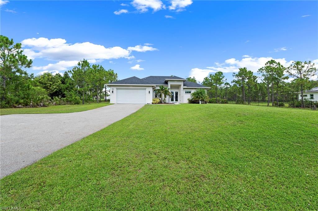 Expansive manicured lawn with mature landscaping and established trees, complemented by a modern single-story residence featuring a white exterior, dark roof, and attached two-car garage accessed via a curved concrete driveway