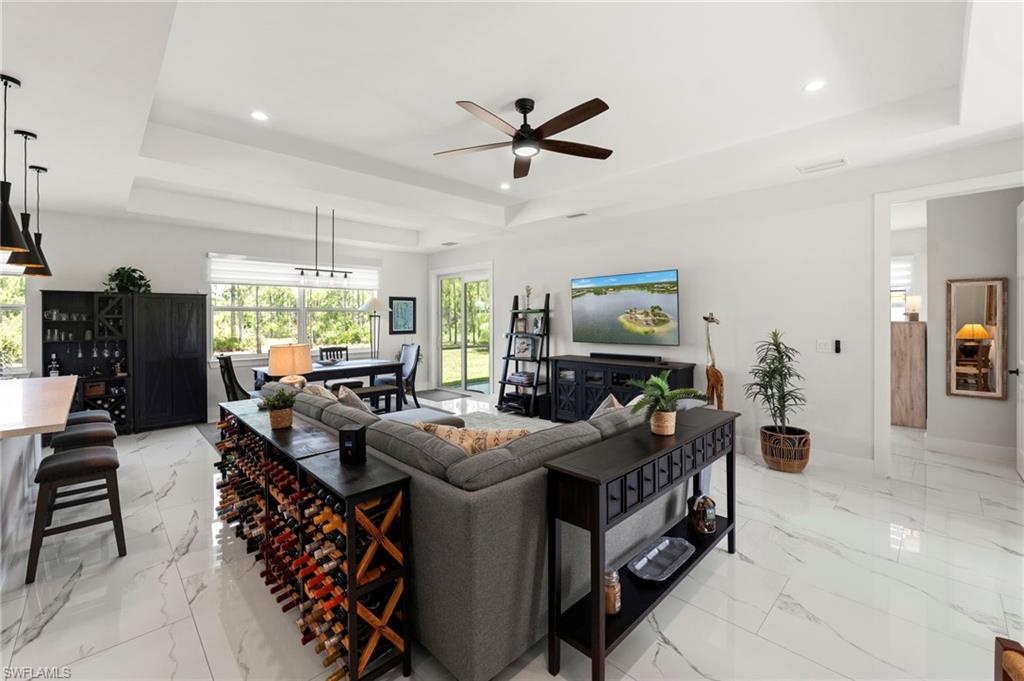 Open-concept living space featuring a coffered ceiling with recessed lighting and ceiling fan, polished tile flooring throughout, and a gray upholstered sectional sofa anchoring the seating area