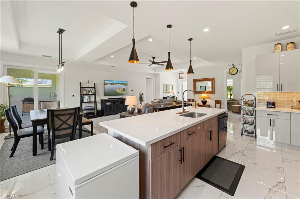 Tray ceiling with recessed lighting, large central island with an integrated sink, white marble-look flooring, and sliding glass doors to the exterior