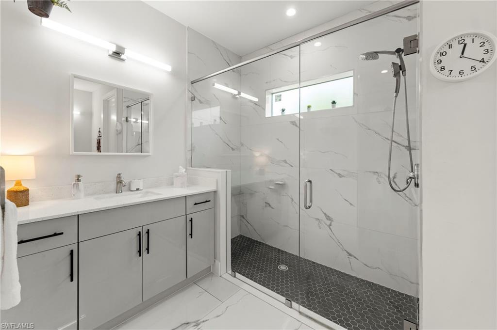 Spa-inspired primary bathroom featuring a frameless glass-enclosed shower with marble-look tile surround, a floating double vanity with integrated sink basins and matte black hardware, quartz countertop, and heated floor tile in the shower area