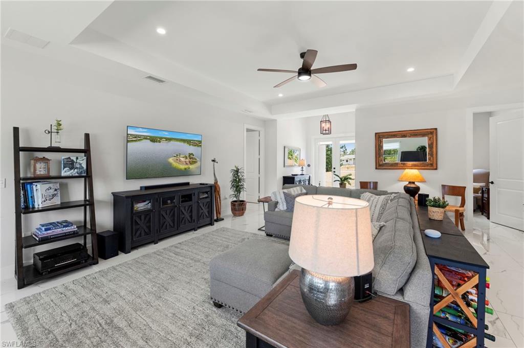 Spacious open-concept living area featuring a coffered ceiling with recessed lighting and ceiling fan, wood-finish flooring throughout, and a built-in media console with dark cabinetry