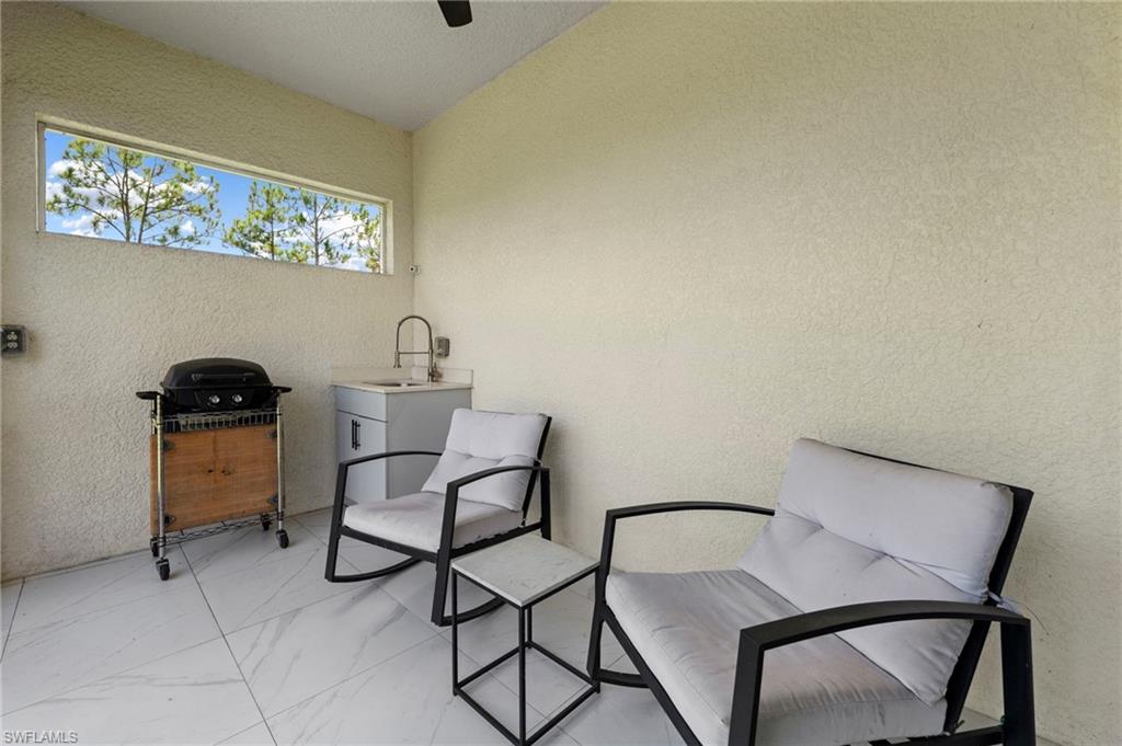 Covered outdoor entertaining space featuring tile flooring, a built-in grill station with wood-finish cabinetry, contemporary seating with black metal frames, and a transom window providing natural light and ventilation