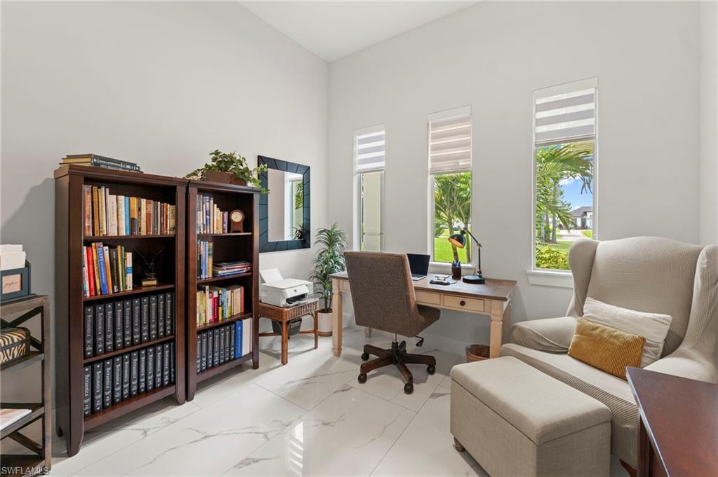 Bright home office featuring built-in wood-finish shelving with glass-front cabinetry, polished concrete flooring, and abundant natural light from three transom windows