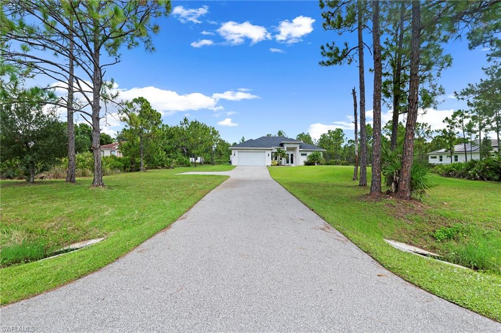 Long paved driveway leading to a single-story residence with an attached garage, surrounded by mature trees and a manicured lawn