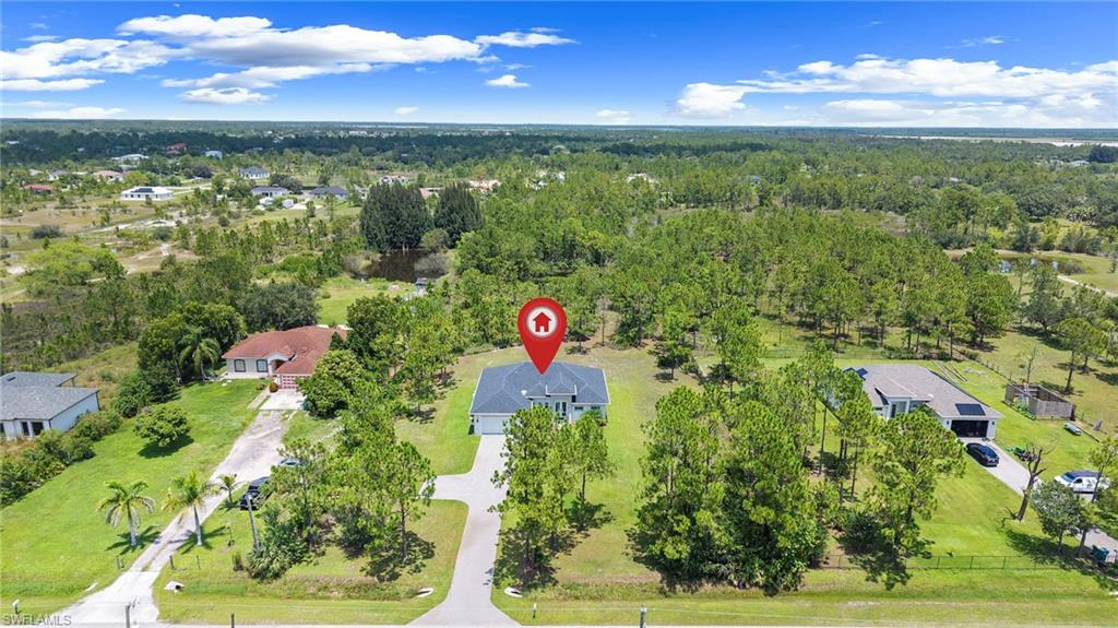 Aerial view showcasing an expansive manicured lawn with mature tree coverage, a sparkling pond, and multiple outbuildings situated on substantial acreage