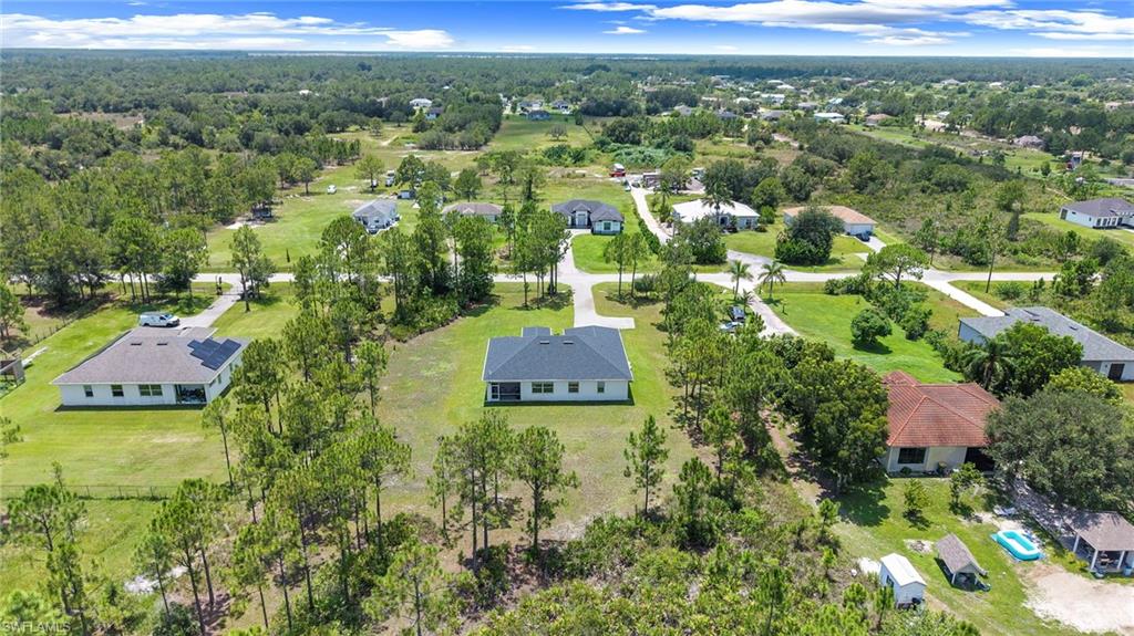 Aerial view showcasing a modern residence situated on expansive grounds with mature landscaping, lush green lawns, and established trees throughout the property