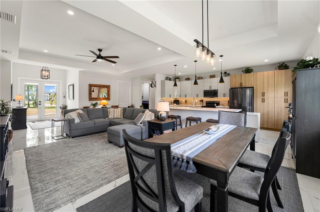 Open-concept living space featuring high ceilings with recessed lighting, an expansive kitchen island with pendant lighting, a dining area with a linear chandelier, and wood-finish cabinetry