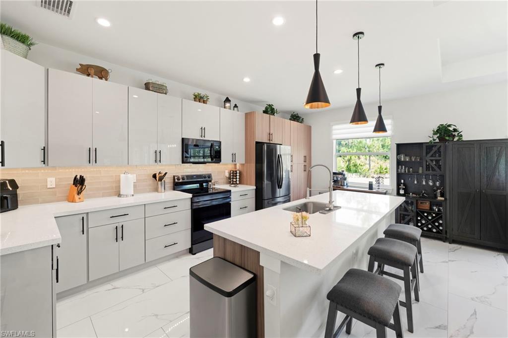 Modern kitchen featuring white cabinetry with integrated hardware, quartz countertops, stainless steel appliances, and a large center island with waterfall edge