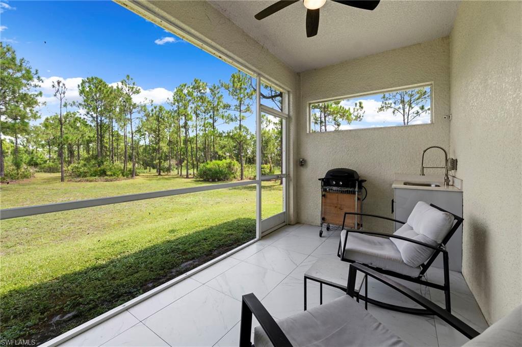 Covered lanai with tile flooring, ceiling fan, and sliding glass doors opening to expansive grounds featuring mature landscaping and manicured lawn
