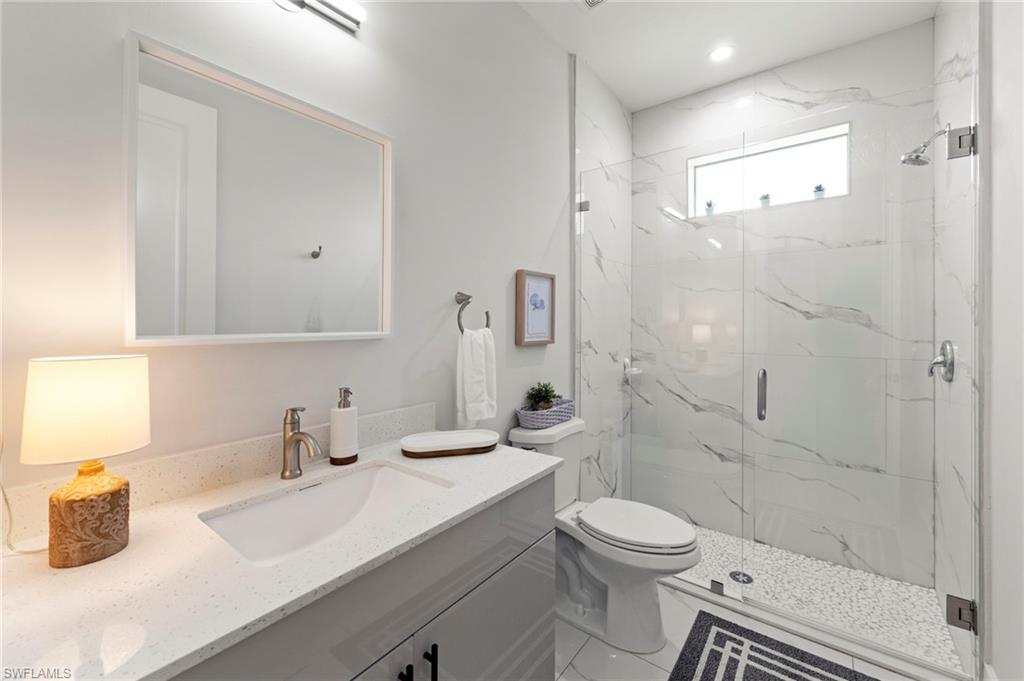 Spa-inspired bathroom featuring a frameless glass shower enclosure with marble-look tile surround, floating vanity with white quartz countertop and rectangular vessel sink, large illuminated mirror, and heated floor with geometric tile pattern