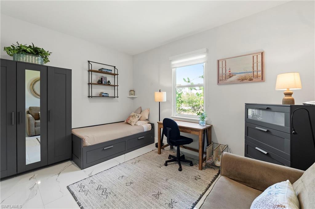 Bright bedroom featuring a wall-mounted desk with integrated workspace, black wardrobe with mirrored doors and storage drawers, and natural light from a large window
