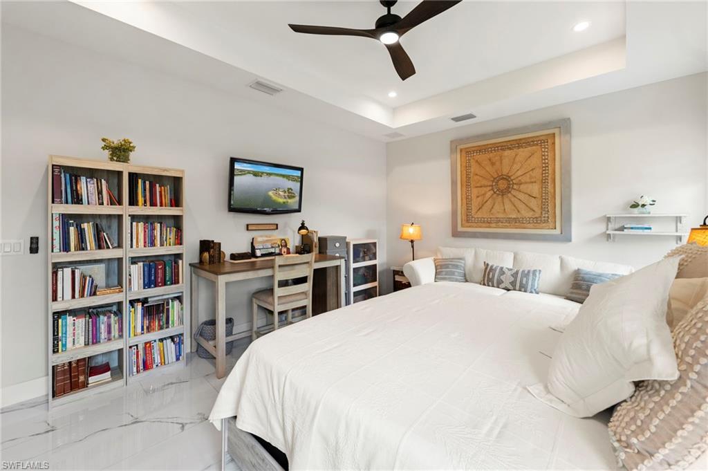 Bright, versatile bedroom suite featuring built-in shelving with extensive storage, dedicated work desk with cabinetry, recessed ceiling lighting, and ceiling fan