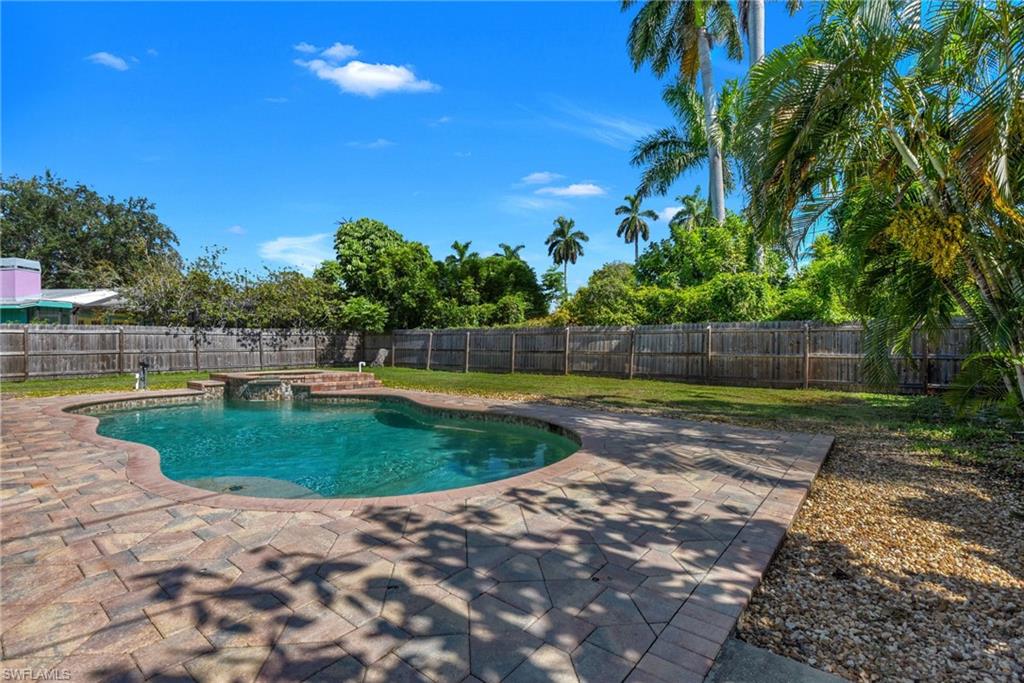 Freeform swimming pool with integrated spa, paver patio, wood fencing, and mature palm trees