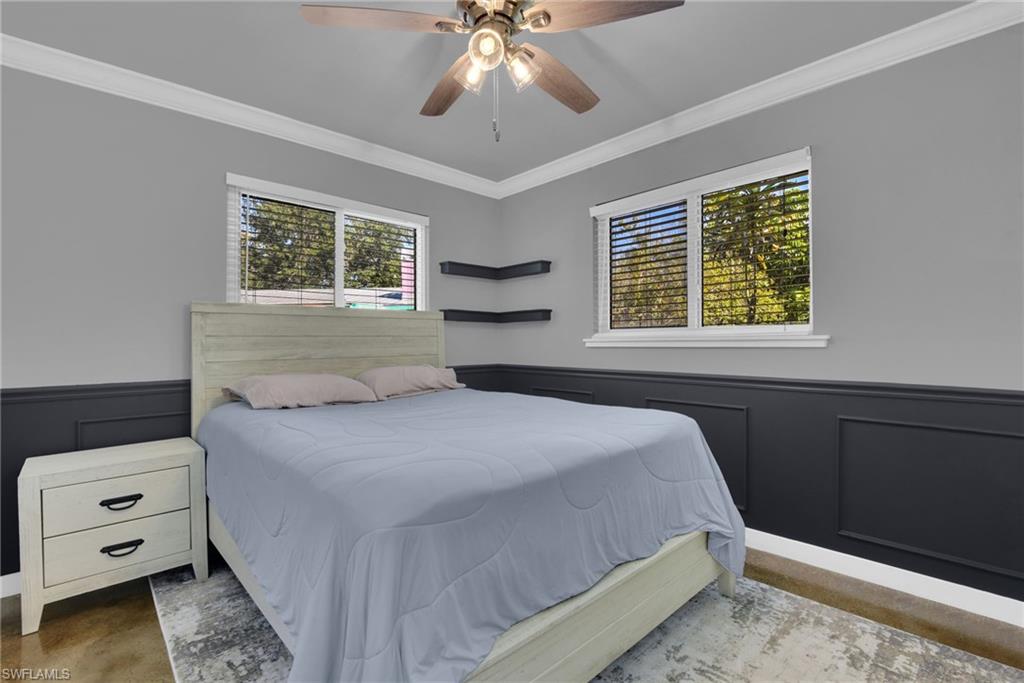 Accent wall paneling, crown molding, wood-finish flooring, two windows with blinds, ceiling fan with integrated lighting