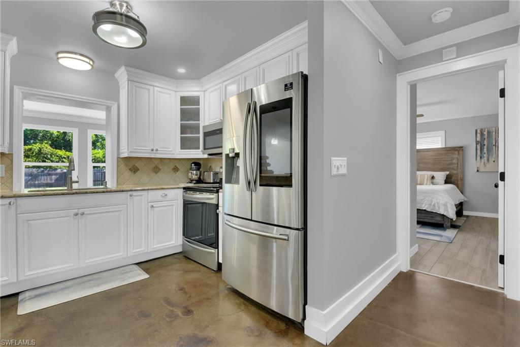 White shaker-style cabinetry with dark hardware, dark hexagonal tile backsplash, and light wood-finish flooring