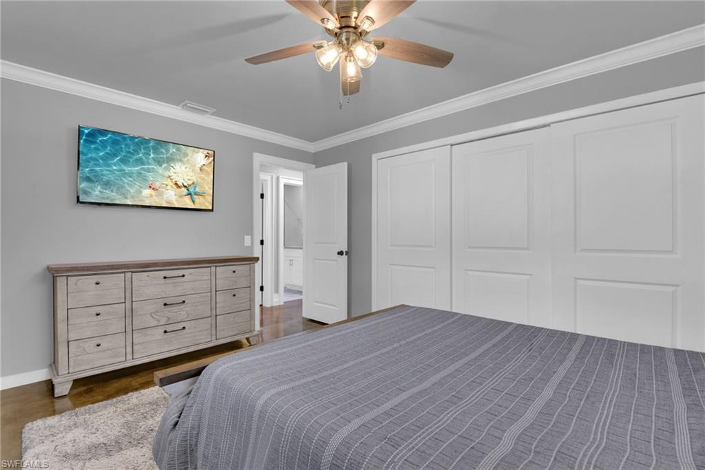 Crown molding, ceiling fan with light fixture, wood-finish flooring, and two paneled sliding closet doors